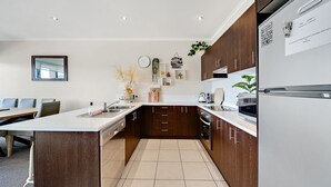 A modern kitchen with a central island, dark wooden cabinets, white countertops, and a built-in oven. - Jasper 4 in the Town Centre with Lake views (Jindabyne)