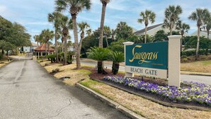 Schild für das Sawgrass Beach Gate, eine private Wohnanlage, mit einer asphaltierten Straße, die zu einem Gebäude mit roten Ziegeln führt.