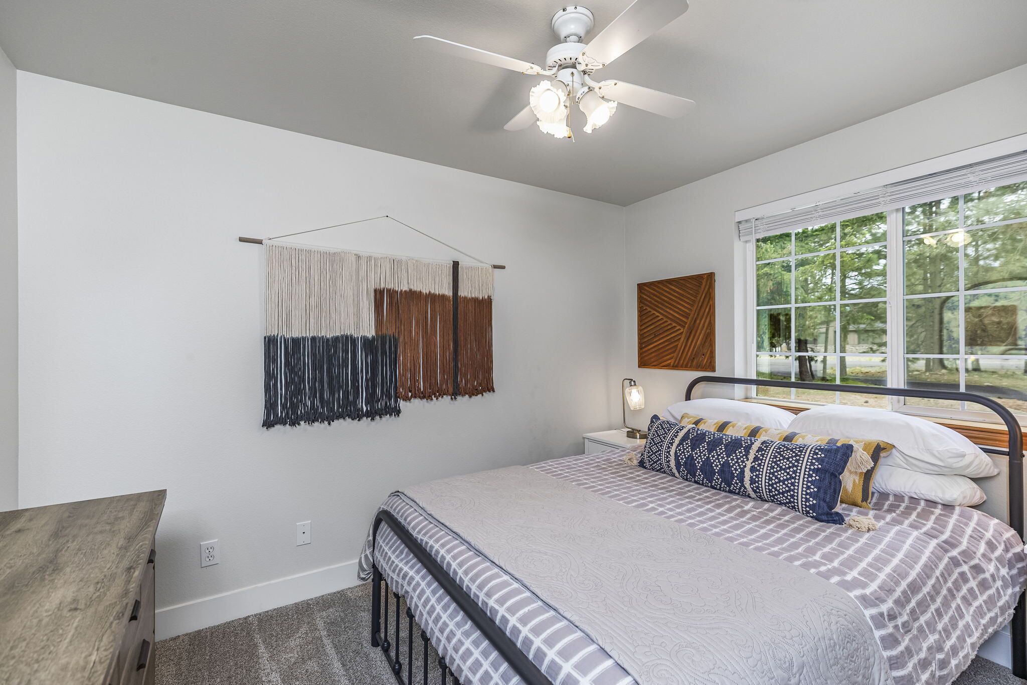 A bedroom with a bed, a ceiling fan, a window, and a wall-mounted light.