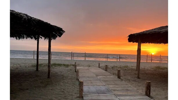 A wooden pathway leading to beach huts with a sunset in the background. - Oceanfront Getaway • Nature • Comfort • Gated Community / Frente al Mar (General Villamil Playas)
