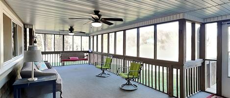 A covered porch with a sofa, chairs, and ceiling fans.