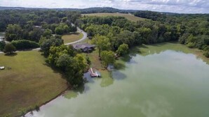 Luchtbeeld van een landgoed aan een meer, met een huis omringd door dichte bomen en een helder pad naar het water.