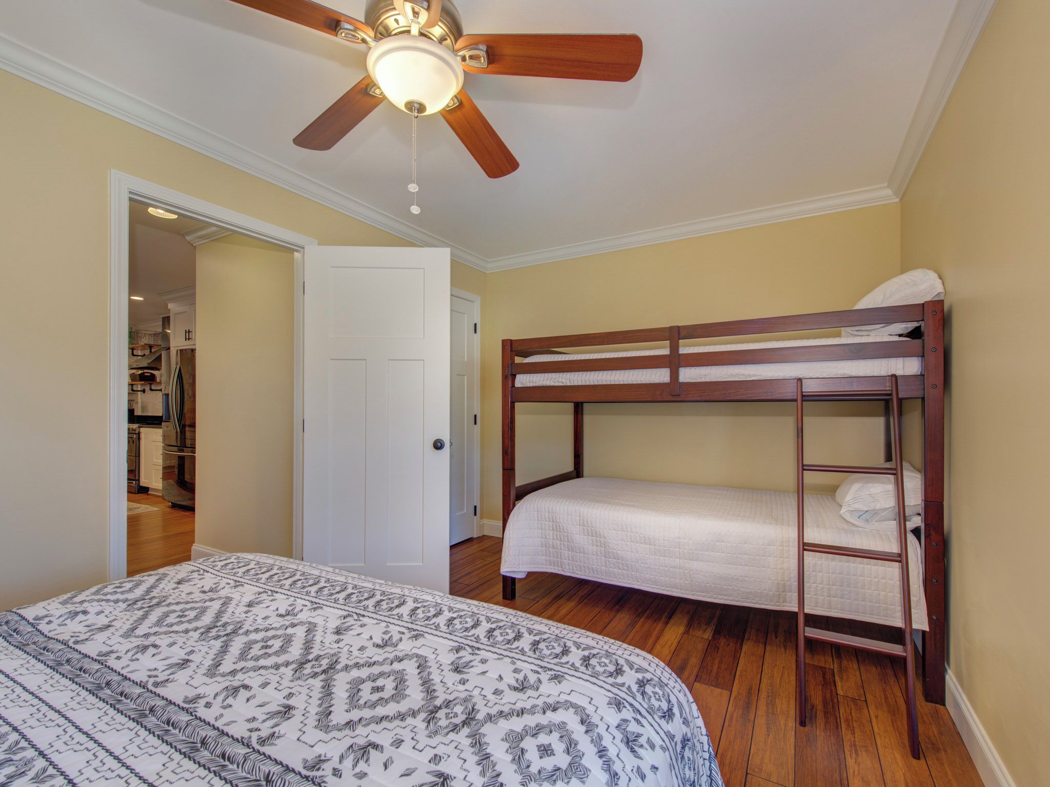 Une chambre avec un lit superposé, un ventilateur de plafond et une couvre-lit à motifs.