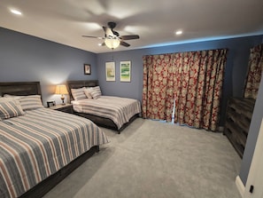 Two beds with striped bedding, a ceiling fan, and a nightstand with a lamp.