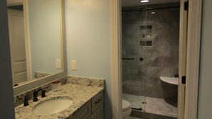 A bathroom with a granite countertop sink, a mirror, and a glass-enclosed shower area. - Reconfigured 2 bedroom, 2 bath condo, walking distance Pinehurst Resort. (Pinehurst)