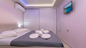 A hotel room with a bed, a flat-screen TV mounted on the wall, and an air conditioning unit on the wall. - Evia s Apartment - New Apartment In Town - Evia s Apartment - New Apartment In Town (Zakynthos)