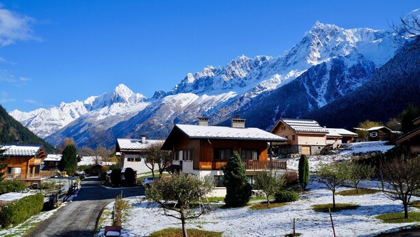 Een bergdorpslandschap bedekt met sneeuw, met houten huizen en een helderblauwe lucht.