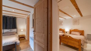 Een slaapkamer met een houten bed, een nachtkastje, een lamp en een deur naar een andere kamer.