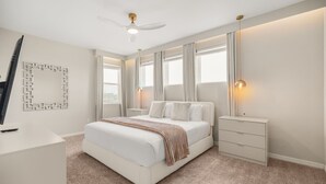 Ein Schlafzimmer mit einem Bett, Nachttischen, einem Deckenventilator und einem am Wand montierten Fernseher.