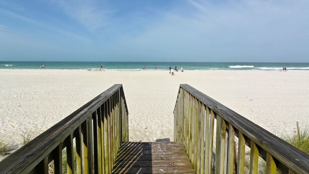 A wooden boardwalk leading to a sandy beach with a clear blue sky. - Beachfront condo with gorgeous view of the gulf. (Bradenton Beach)