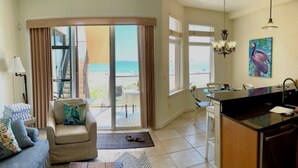A living room with a sofa, armchair, and coffee table, a kitchen with a sink and stove, and a balcony with a view of the ocean. - Beachfront condo with gorgeous view of the gulf. (Bradenton Beach)