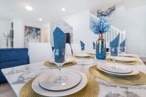 A dining table set with white plates, gold placemats, and blue napkins.