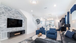 Een moderne woonkamer met een flatscreen televisie, blauwe gestoffeerde fauteuils, een zwarte leren bank en een trap naar de bovenverdieping.