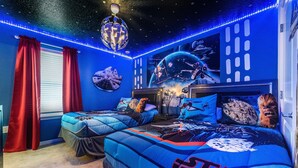 Un dormitori temàtic de Star Wars amb dos llits, cortines vermelles i decoració mural amb motius espacials.