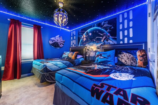 A Star Wars-themed bedroom with two beds, red curtains, and space-themed wall art.
