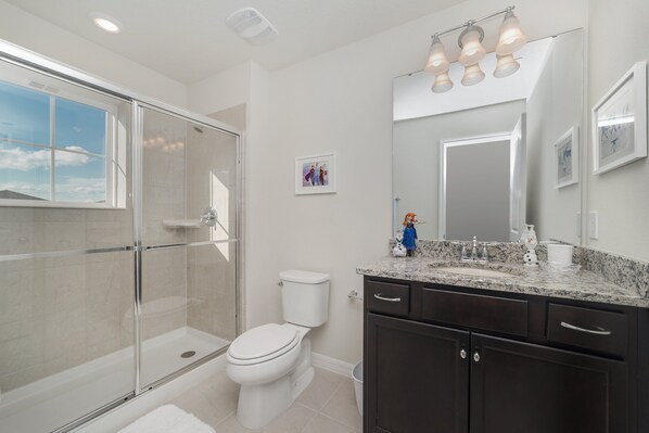 A modern bathroom with a glass-enclosed shower, a toilet, dark cabinets, and a granite countertop.