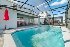 A swimming pool with a glass enclosure, red chairs, and a red umbrella.