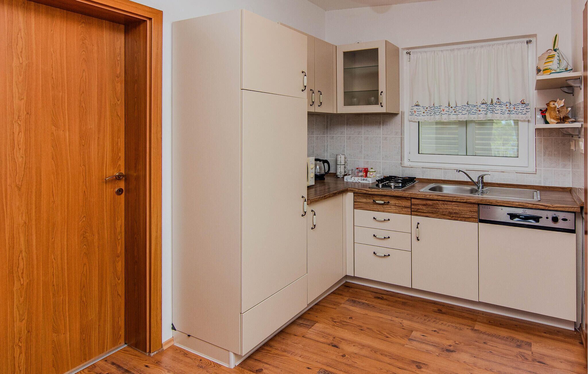 A compact kitchen with a wooden door, white cabinets, a built-in oven, and a window with a curtain.