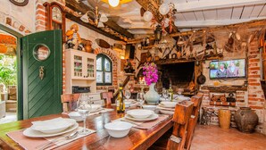 Un coin repas rustique avec une longue table en bois dressée pour un repas, entouré de murs en briques et agrémenté de divers objets décoratifs.