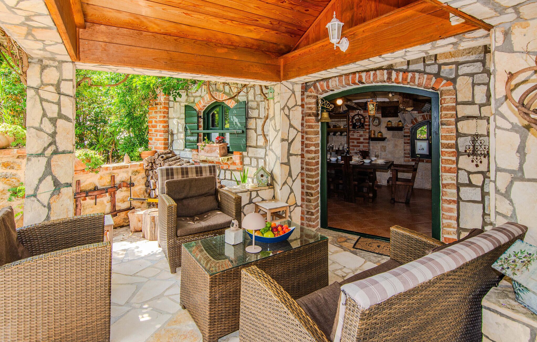 An outdoor patio area with wicker furniture, a stone wall, and a brick fireplace.