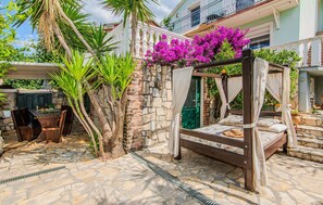 A wooden bed with a canopy, surrounded by a stone patio, and a balcony with a view of the building. - Gorgeous home in Maslenica (Maslenica)