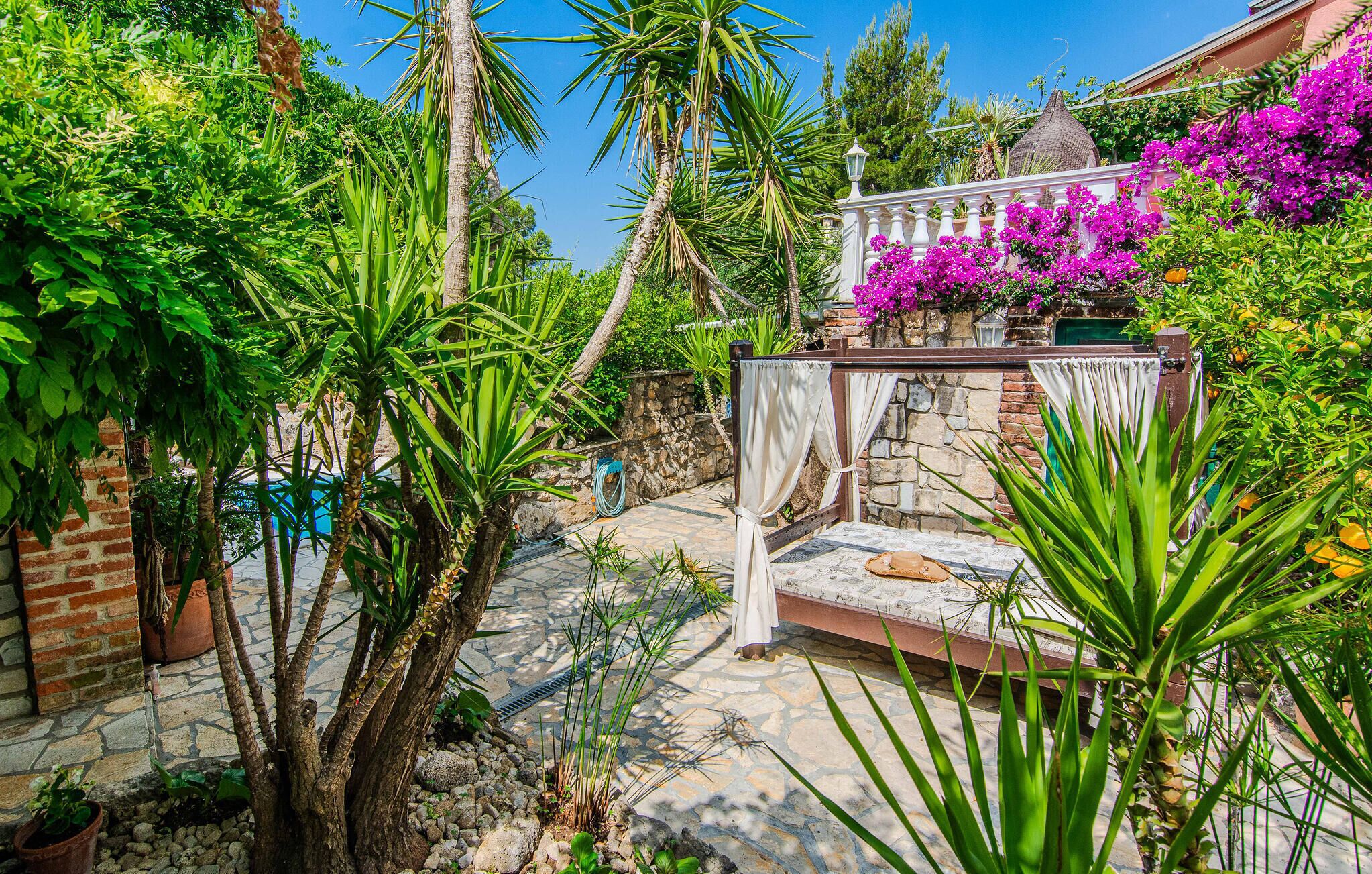 A garden with a stone bench, lush greenery, and a white railing with purple flowers.