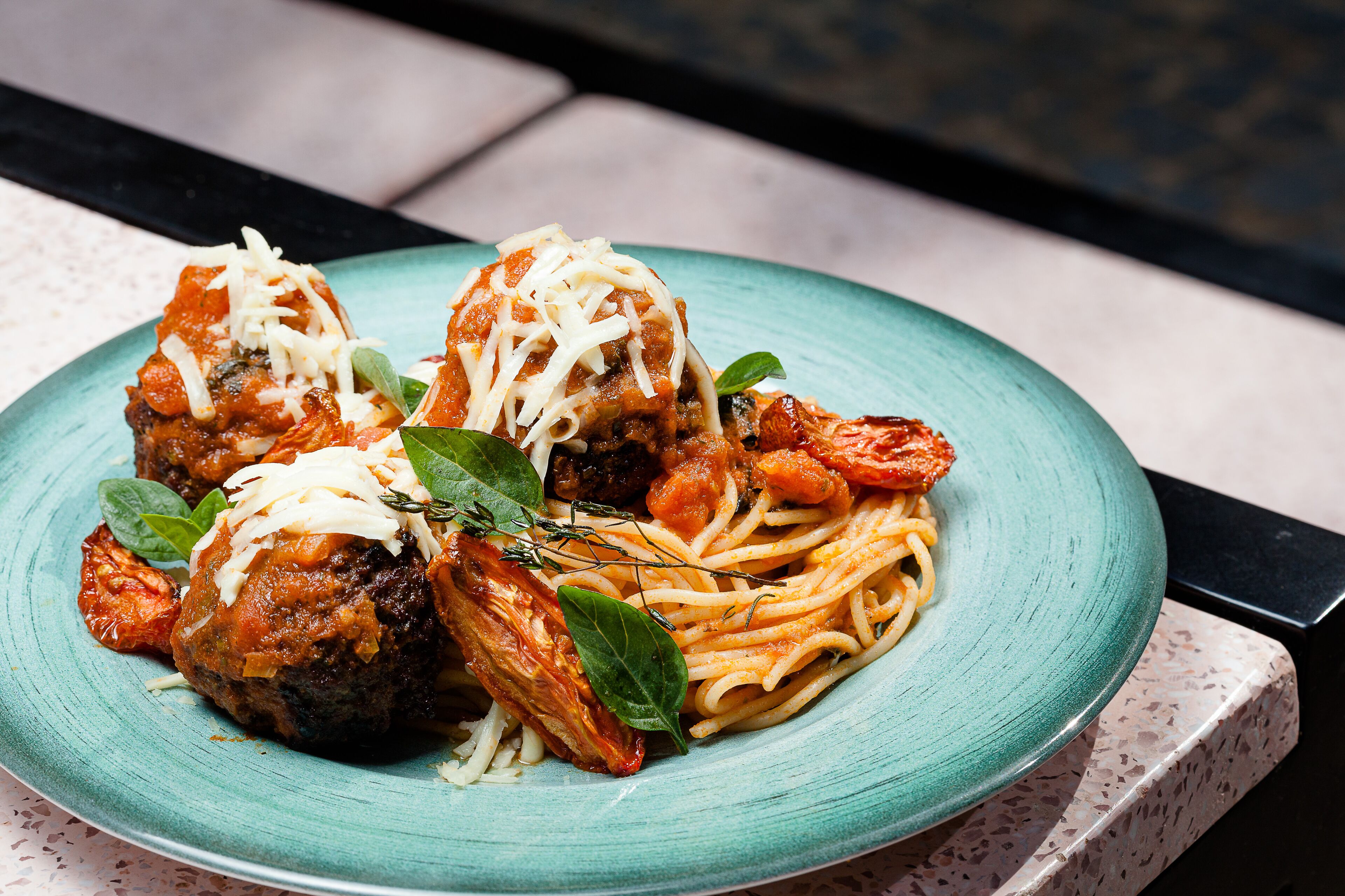 Un piatto di polpette e spaghetti con formaggio e erbe aromatiche.
