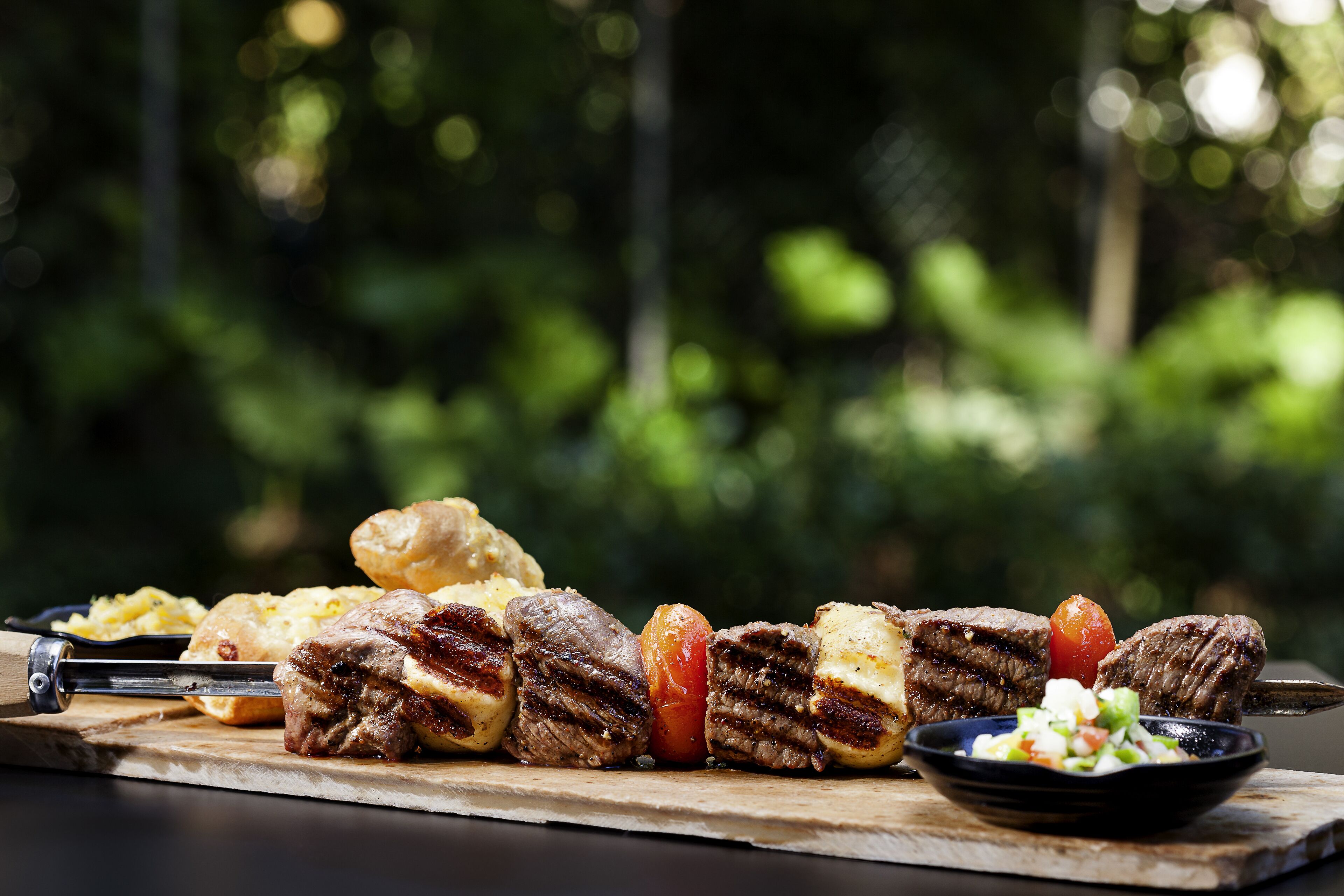A wooden cutting board with grilled meat, vegetables, and a bowl of salad.