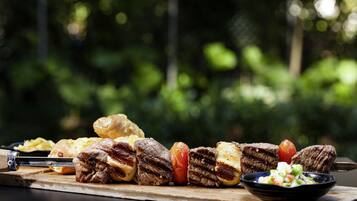 A wooden cutting board with grilled meat, vegetables, and a bowl of salad.