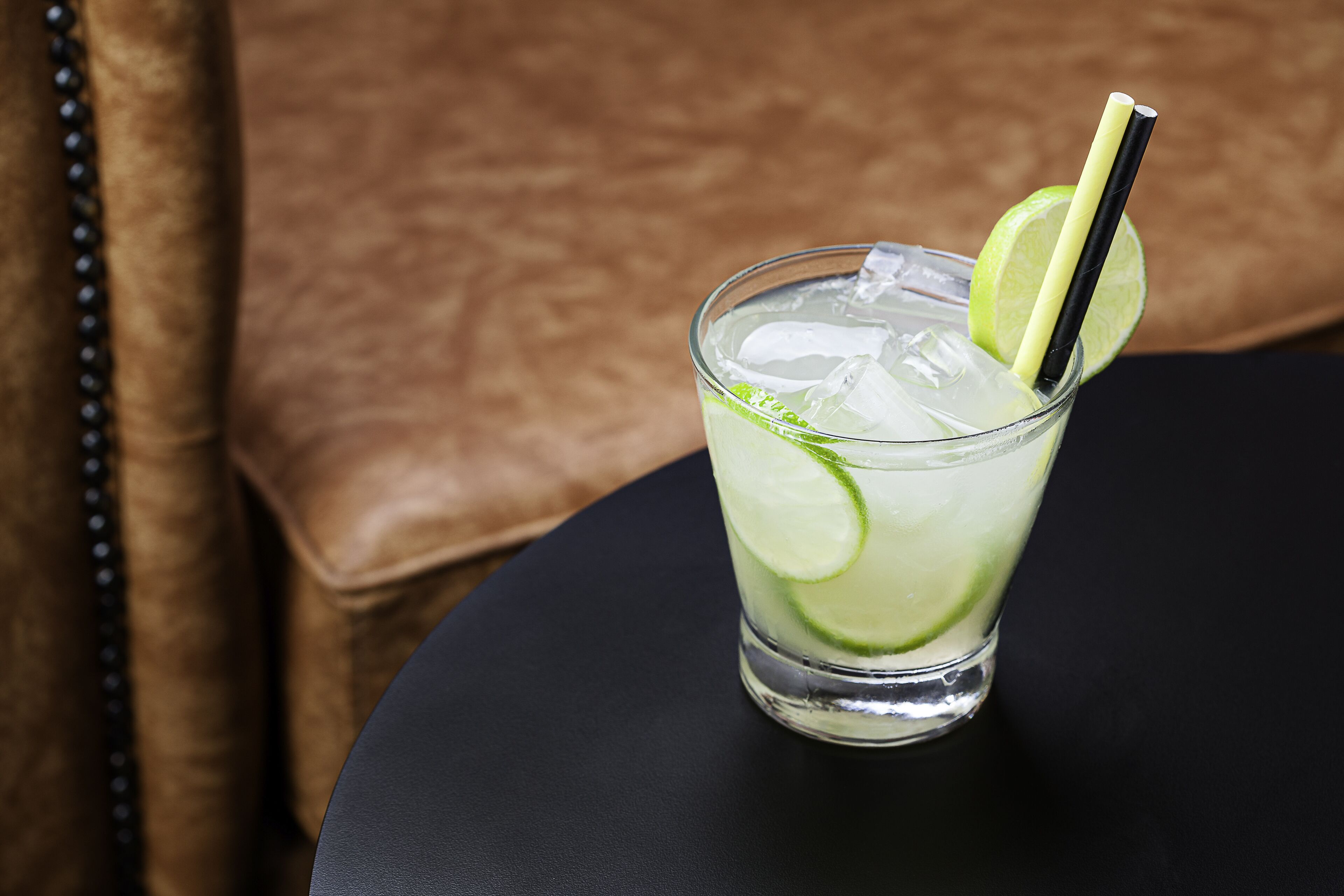 A glass with a lime slice and a straw on a black table.