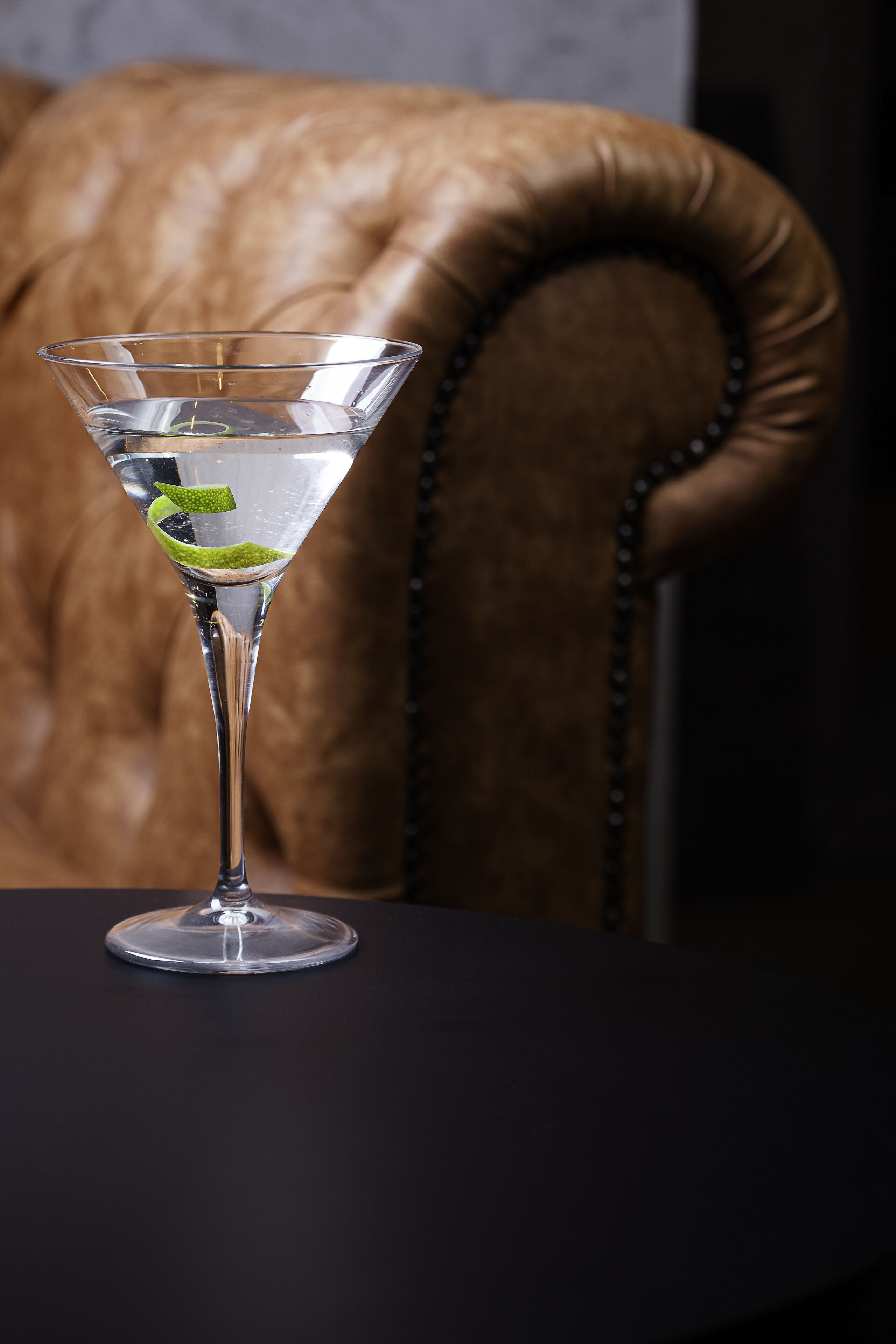 A martini glass with a lime twist on a dark table.
