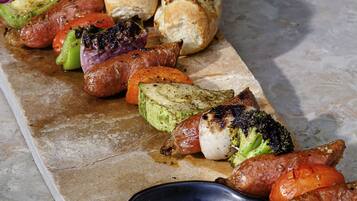 A stone table with grilled sausages, vegetables, and bread.