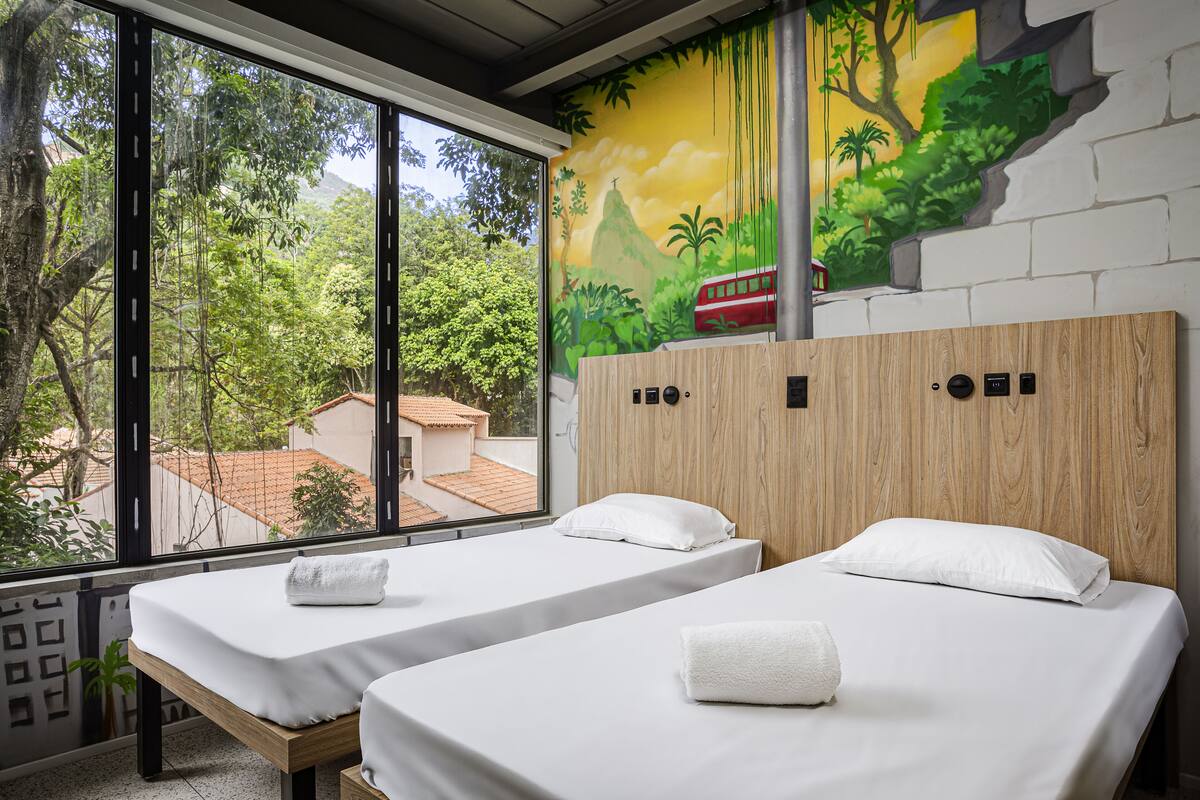 A room with two beds, large windows, and a mural of a jungle scene.