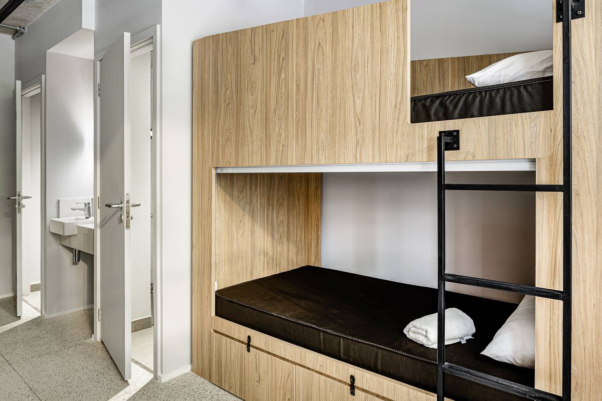 A bunk bed with a wooden headboard, a black ladder, and a white pillow.