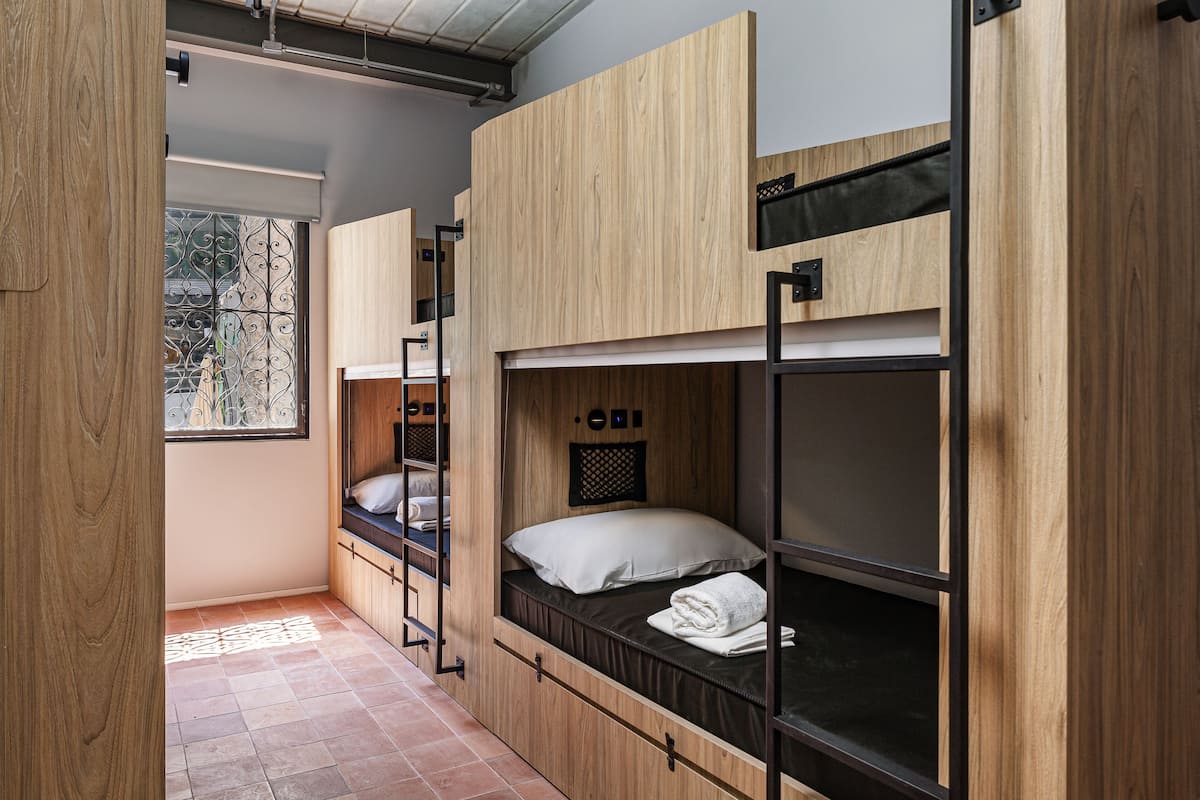 A compact room with bunk beds, wooden walls, a window with decorative ironwork, and a tiled floor.