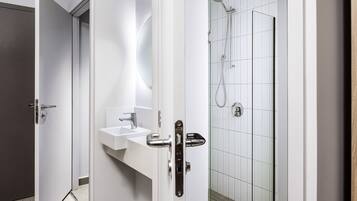 A modern bathroom with a white sink, a glass shower enclosure, and a door with a silver handle.