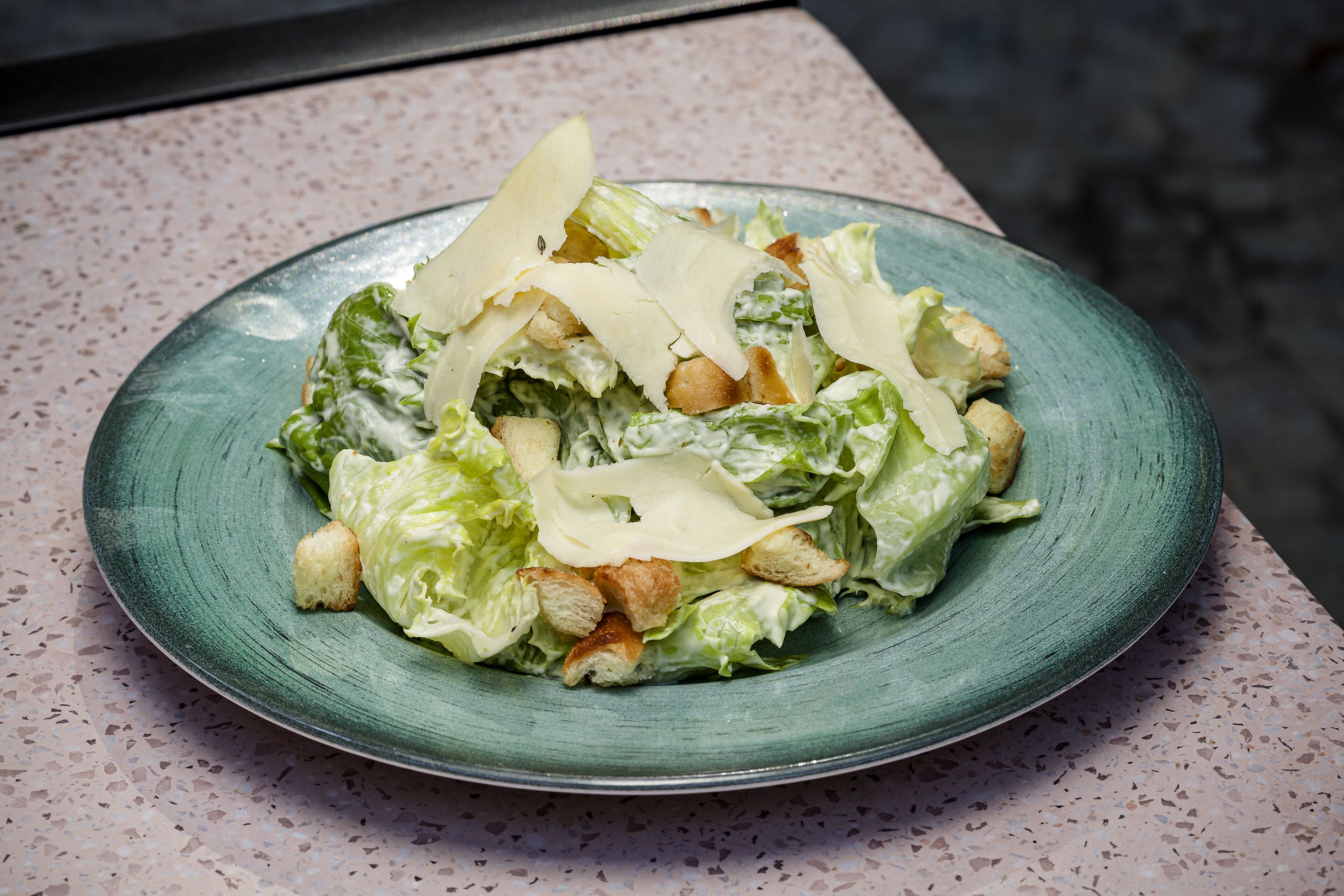 A green ceramic plate with a salad on a speckled countertop.
