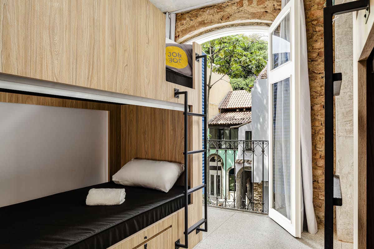 A bunk bed with a black mattress and white pillow, a wooden headboard, and a small shelf with a yellow object.