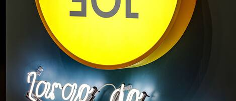 Una señal amarilla circular con el texto 'JOGO' y una señal de neón debajo que dice 'Largo do Botânico'.