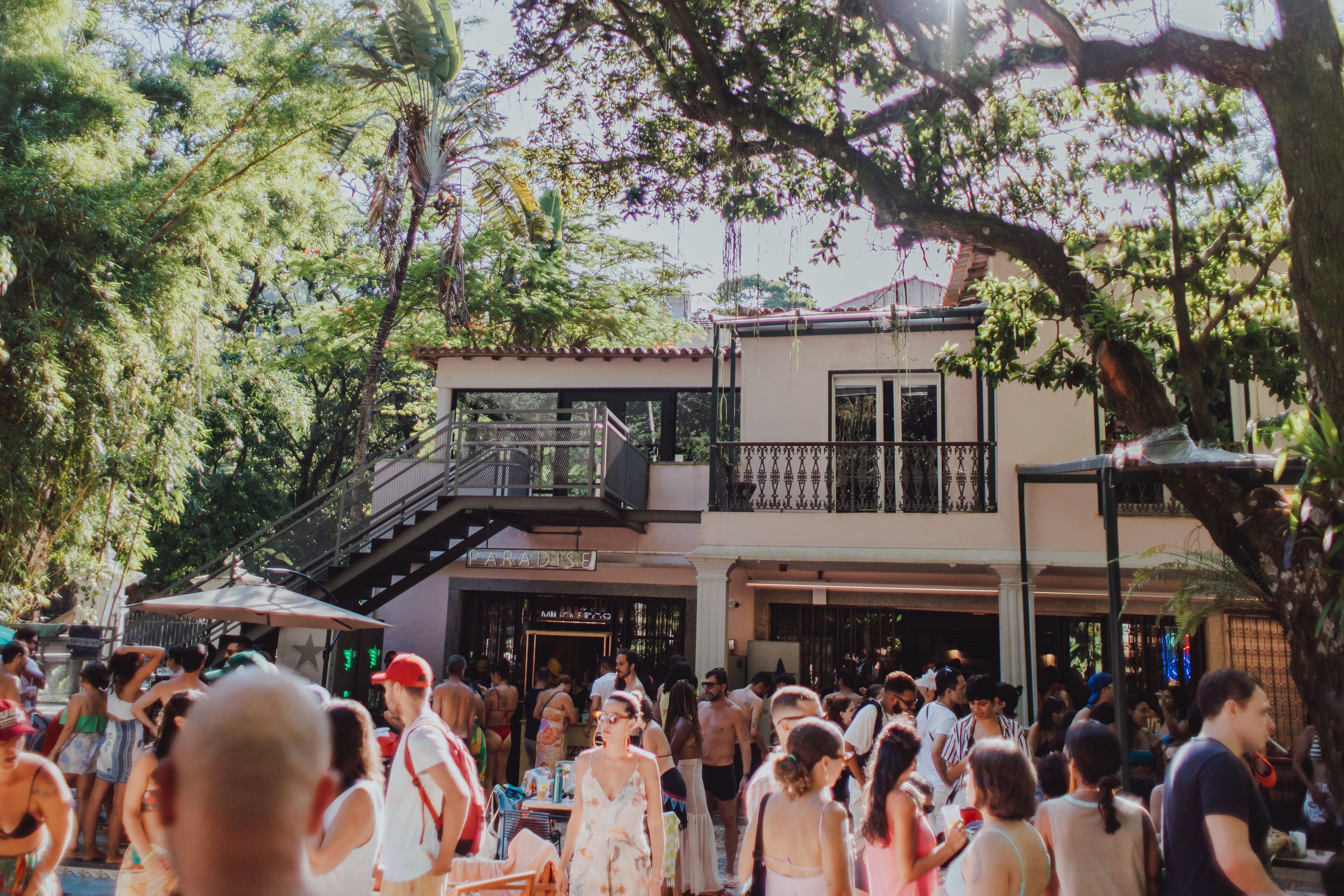 A crowded outdoor area with a building that has a balcony and a staircase.
