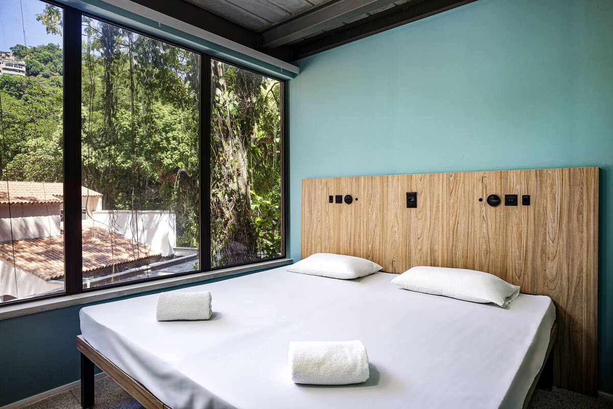 A bedroom with a large window, a wooden headboard, and two white towels on the bed.