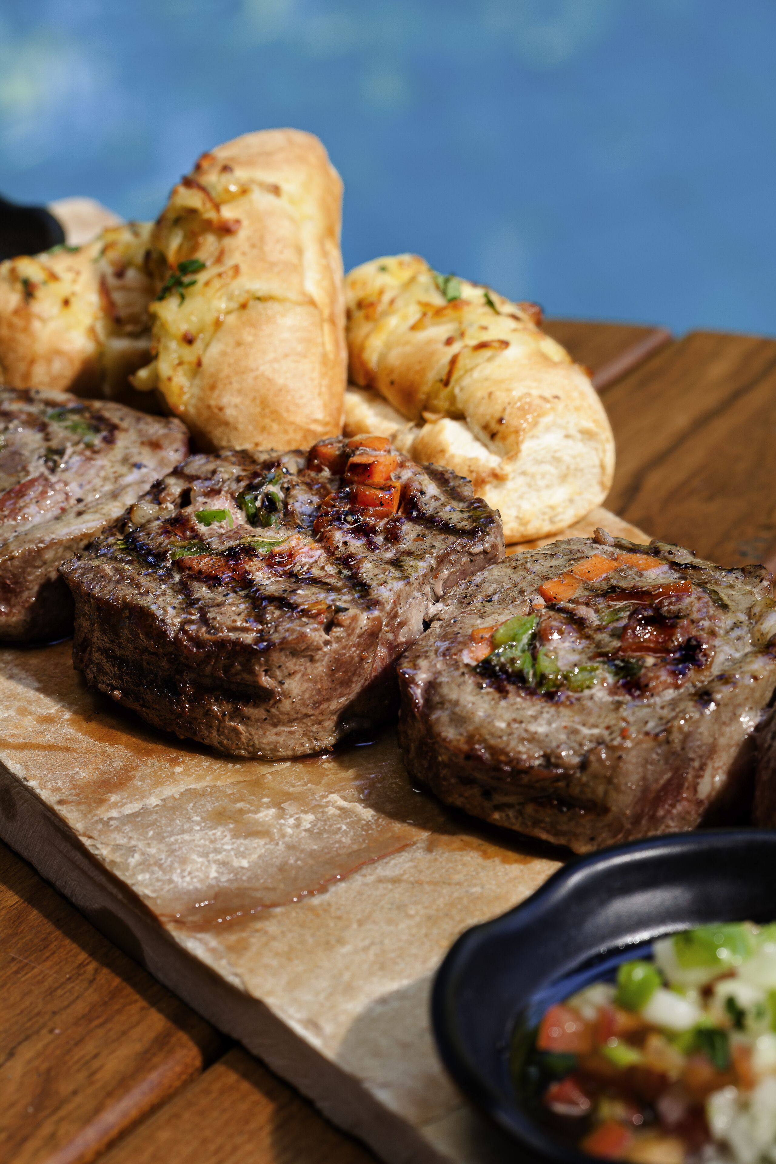 A wooden table with a serving of meatloaf, rolls, and a small bowl of salsa.