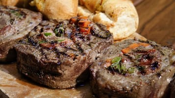A wooden table with a serving of meatloaf, rolls, and a small bowl of salsa.