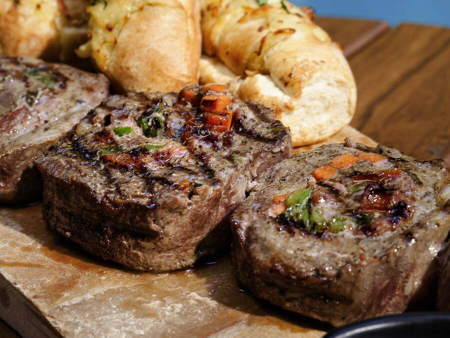 A wooden table with a serving of meatloaf, rolls, and a small bowl of salsa.
