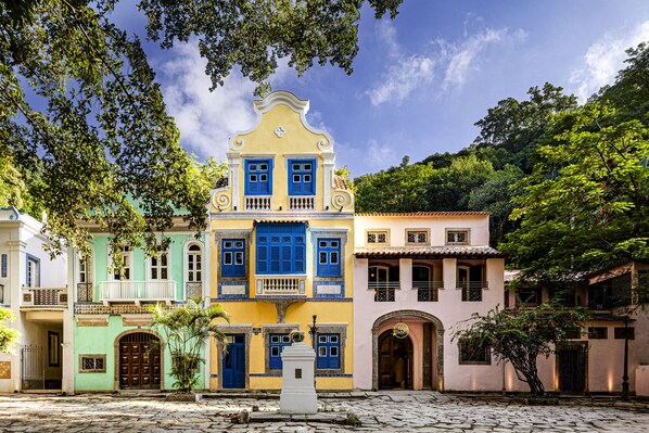 Un bâtiment aux couleurs vives, doté d’un balcon central et d’une cour pavée de pierres.