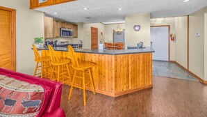 A kitchen with wooden cabinets, a microwave, and a dining area with wooden chairs.