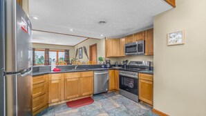A modern kitchen with wooden cabinets, stainless steel appliances, and a stone tile floor.