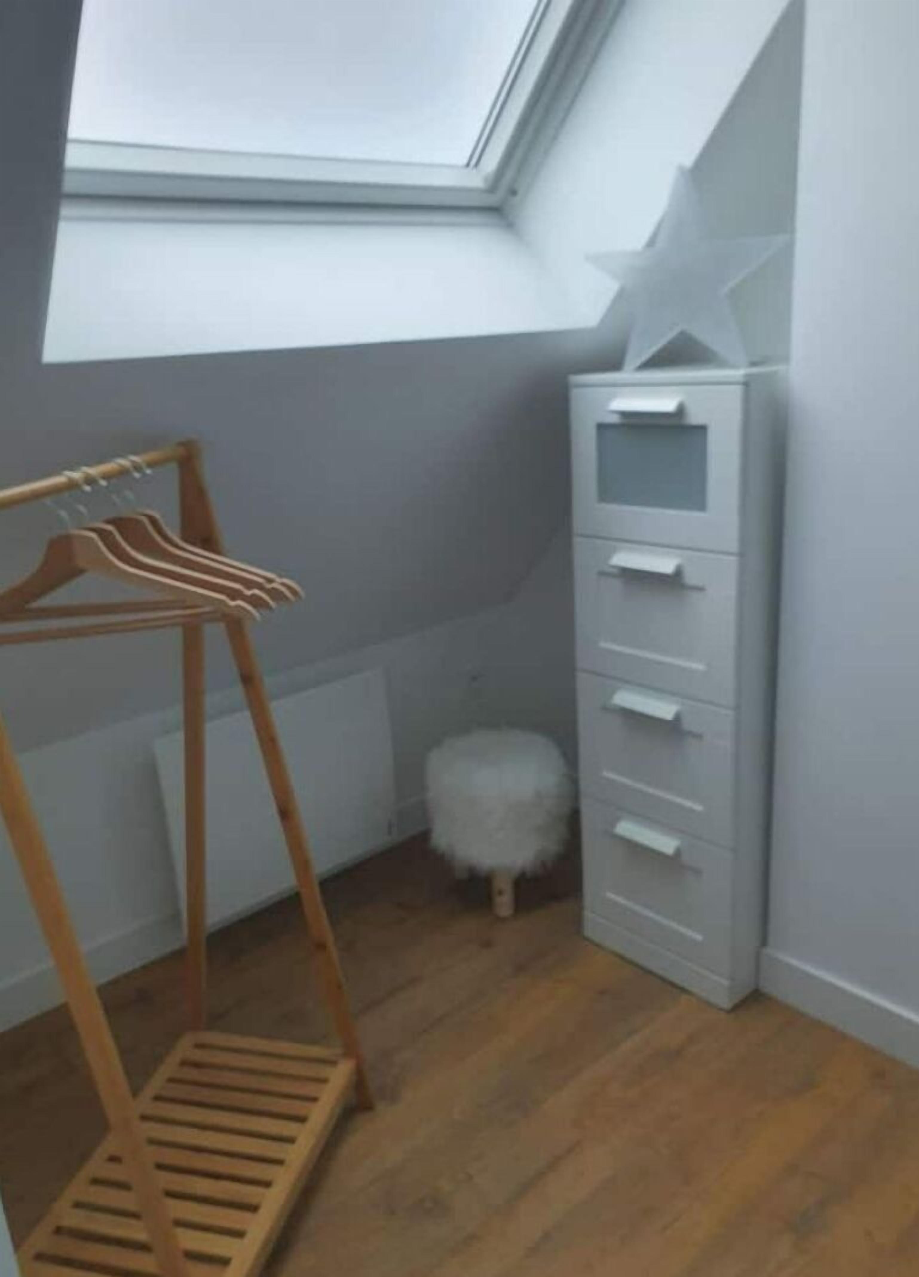 A room with a skylight, a wooden hanger rack, a white storage unit, and a fluffy white stool.