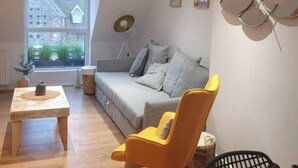 Ein modernes Wohnzimmer mit einer Couch, einem gelben Sessel, einem Couchtisch und einem Fenster mit Blick auf Gebäude.