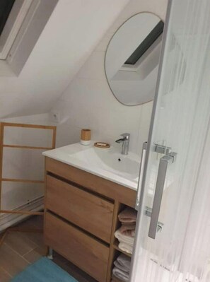 Ein kleines, modernes Badezimmer mit Oberlicht, weißem Waschbecken, Holzschrank und Handtuchhalter.